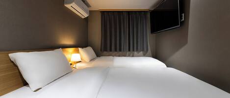 A hotel room with a bed, a TV mounted on the wall, an air conditioning unit, and a window with curtains.