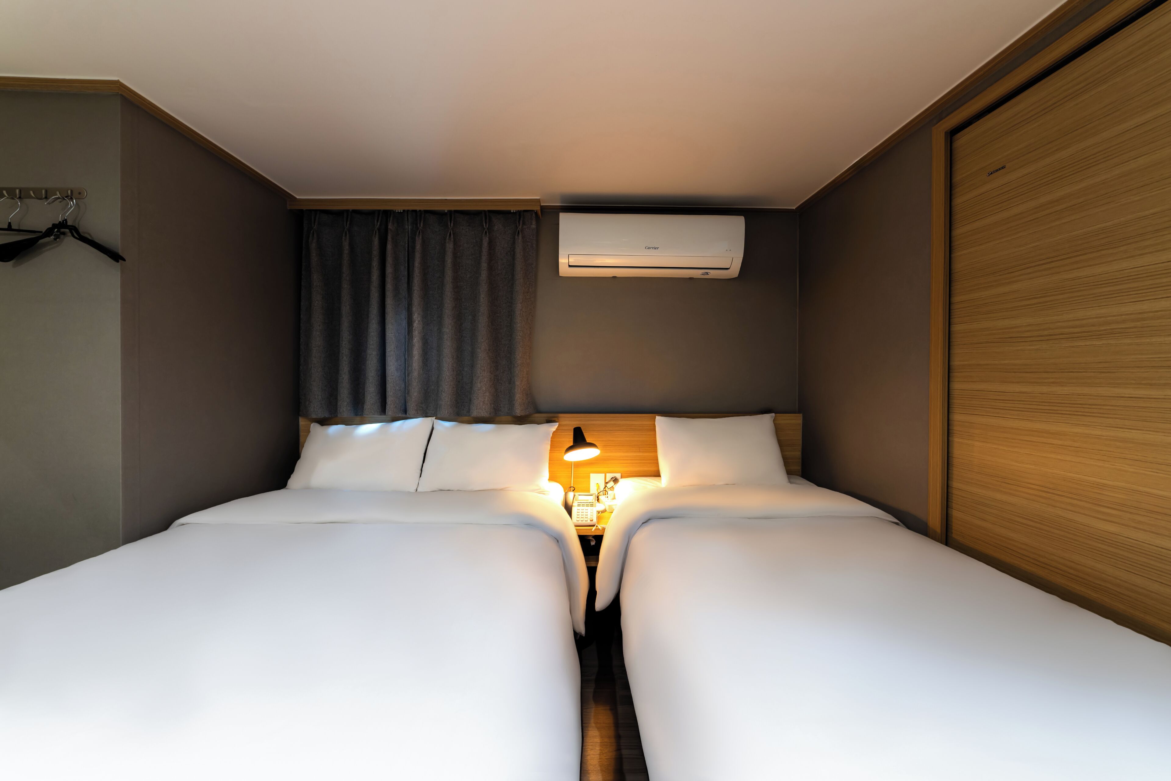 A double bed with a bedside table and lamp, an air conditioning unit, and a wooden wardrobe.