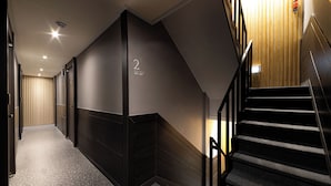A modern hotel corridor with a dark interior, a staircase, and a wooden wall with a number sign. - About Stay Seoul Station (Seoul)