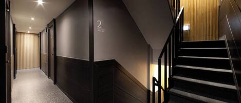 A modern hotel corridor with a dark interior, a staircase, and a wooden wall with a number sign.