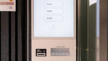 Een digitale kiosk met een scherm waarop een taalmenu, een sleuf voor een hotelpasje en een kaartlezer voor contante en kaartbetalingen staan.