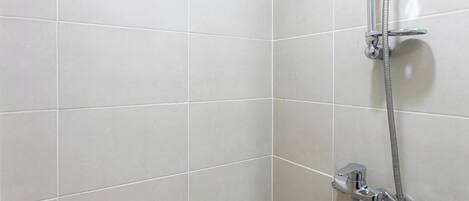 A shower area with a handheld showerhead and a fixed wall-mounted showerhead.
