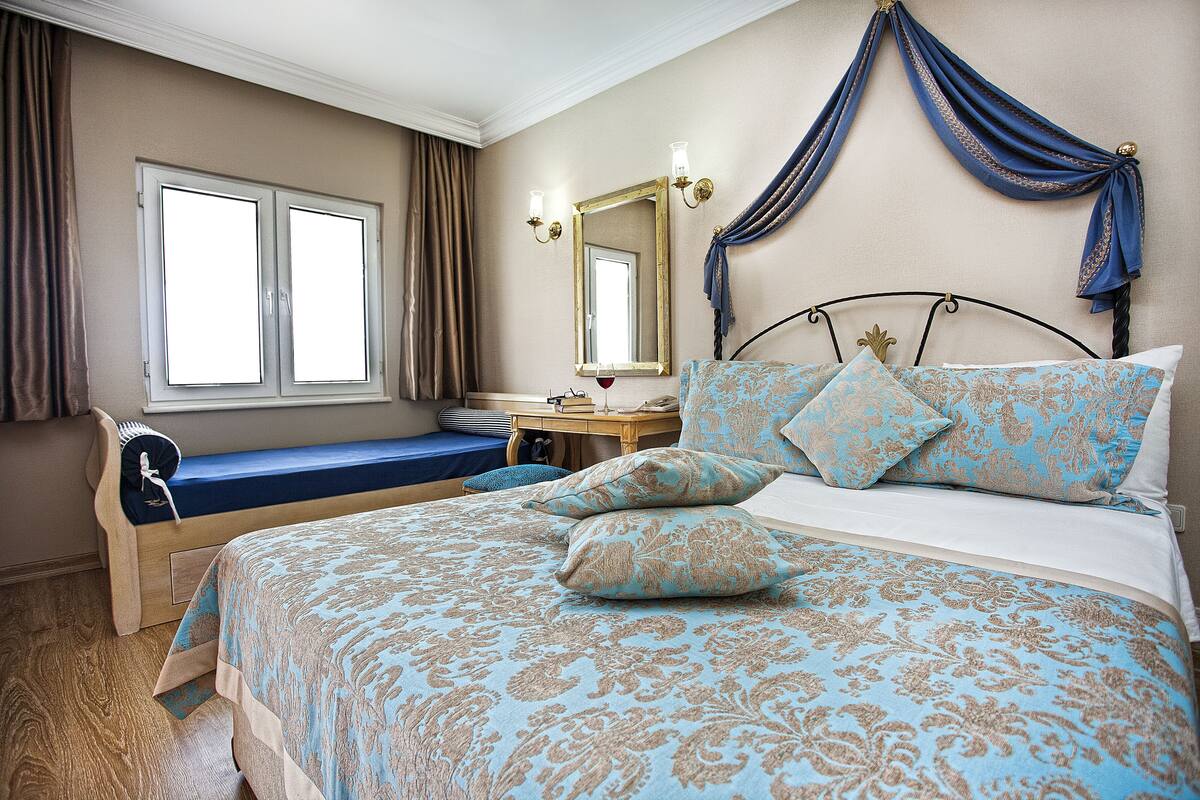 A bedroom with a large bed, a bedside table, a mirror, and a window with curtains.