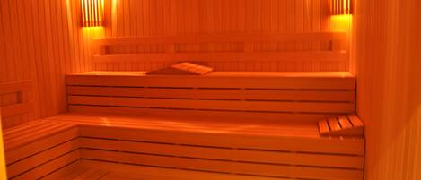 Sauna, jossa on puiset penkit ja seinät sekä kaksi seinälle asennettua valaisinta.
