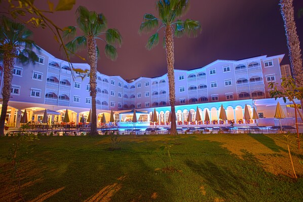 Un hotel con piscina, palmeras y mobiliario exterior.