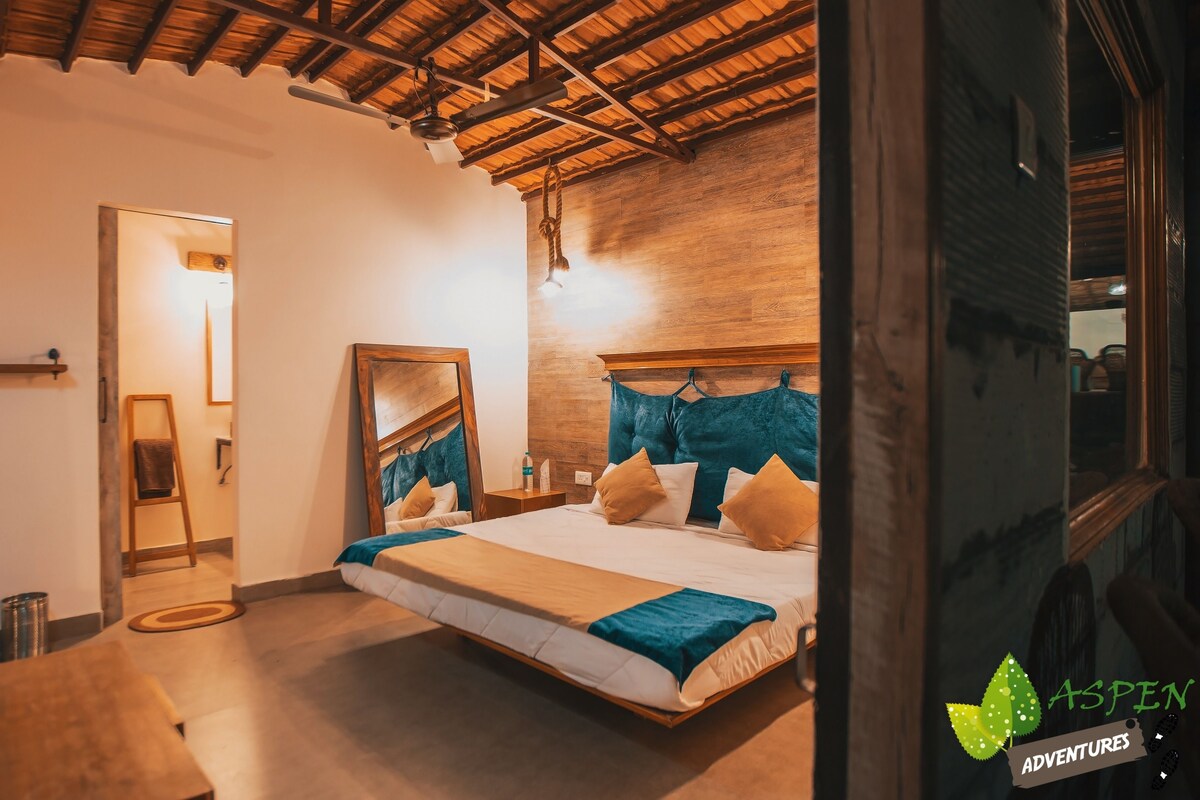 Ein Schlafzimmer mit Holzbalkendecke, einem Bett mit blau-beiger Bettwäsche, einer Holzleiter und einem Spiegel an der Wand.