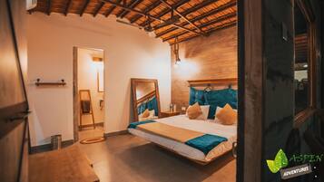 Ein Schlafzimmer mit Holzbalkendecke, einem Bett mit blau-beiger Bettwäsche, einer Holzleiter und einem Spiegel an der Wand.
