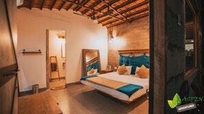 Ein Schlafzimmer mit Holzbalkendecke, einem Bett mit blau-beiger Bettwäsche, einer Holzleiter und einem Spiegel an der Wand.