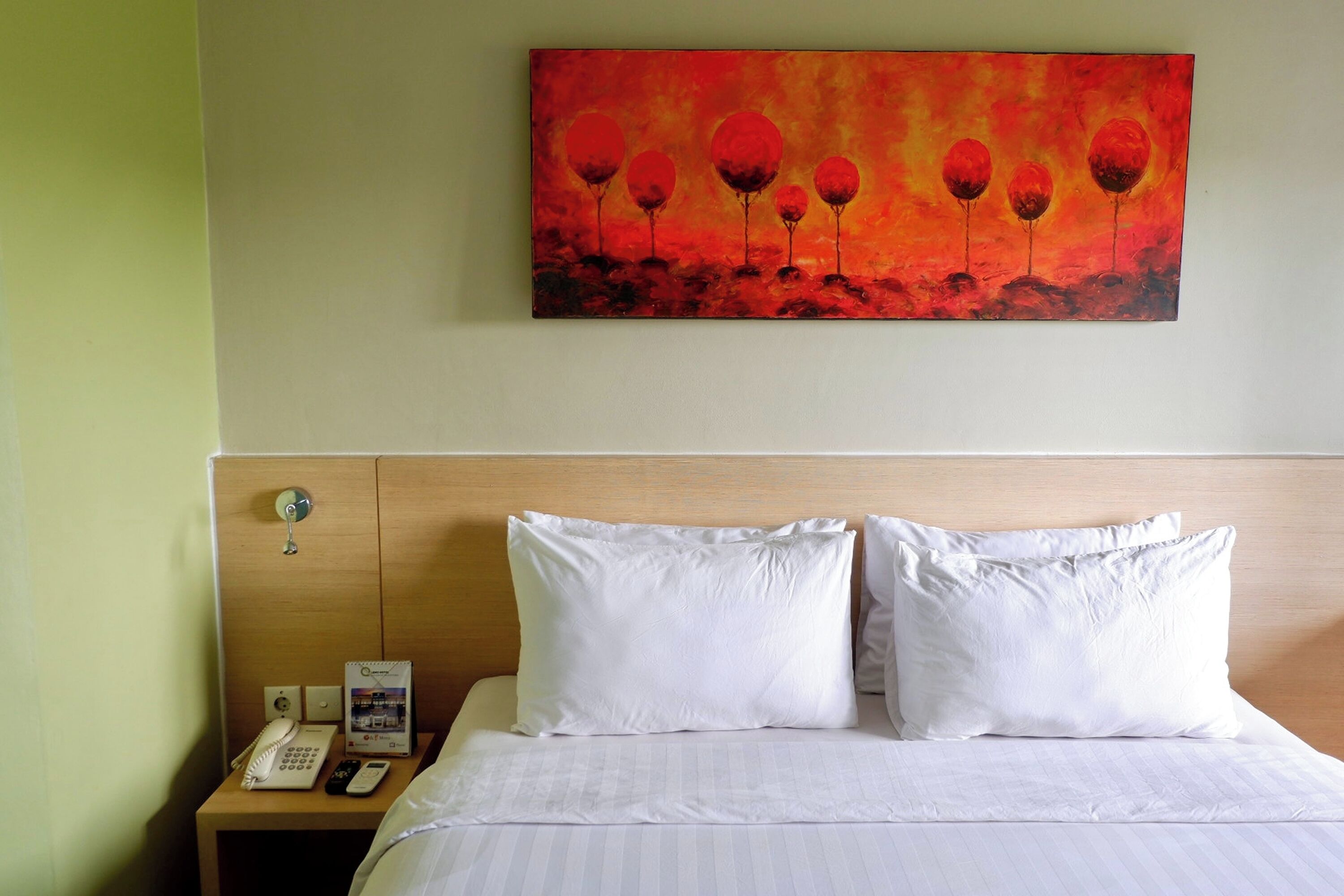 Habitación de hotel con cama, almohadas blancas, mesita de noche con teléfono y un cuadro de flores rojas en la pared.