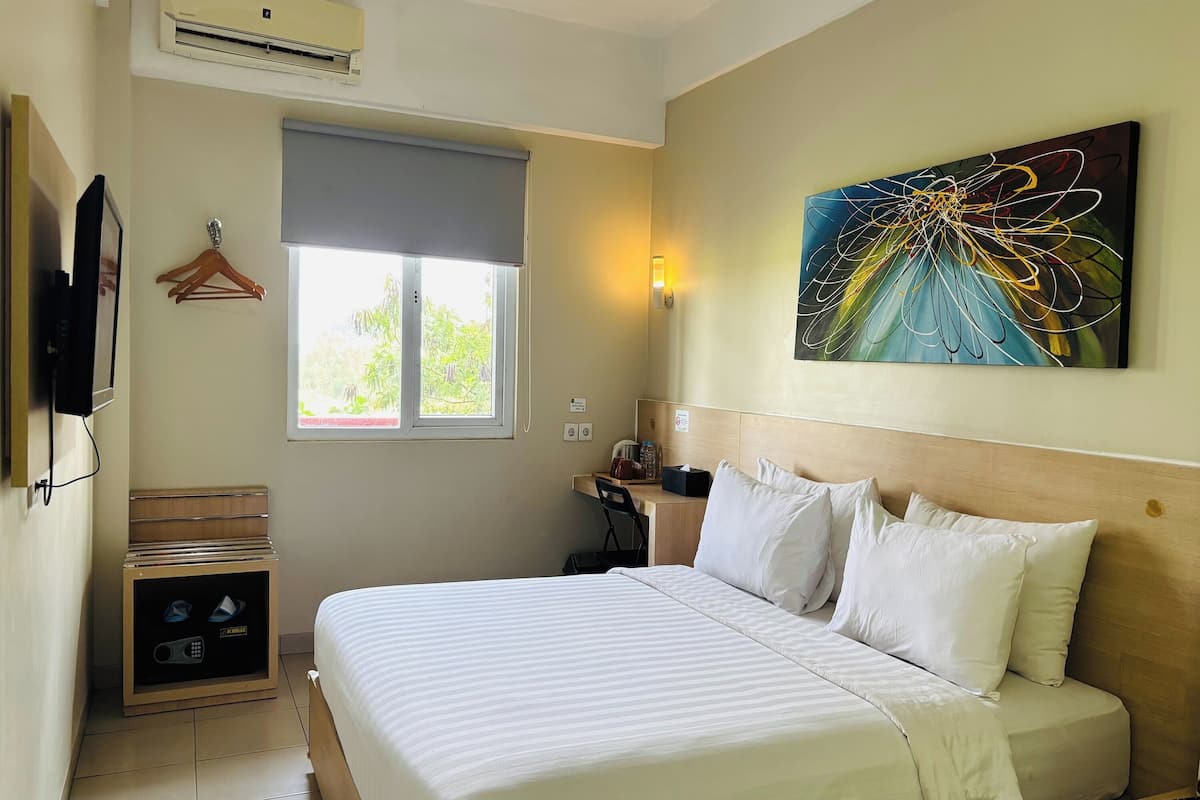 A hotel room with a bed, a desk, a chair, a TV, a wardrobe, and a window with a view of greenery.