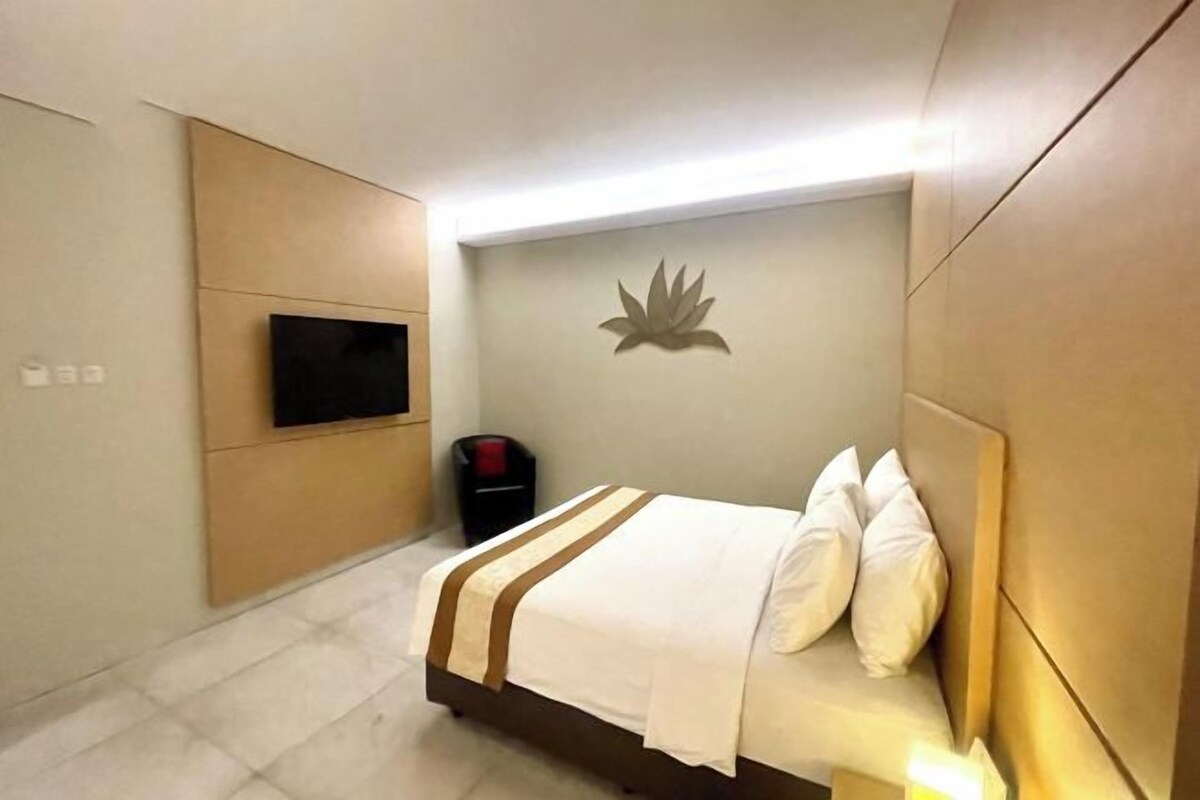 A modern hotel room with a bed, a mounted TV, and a wall-mounted light fixture.