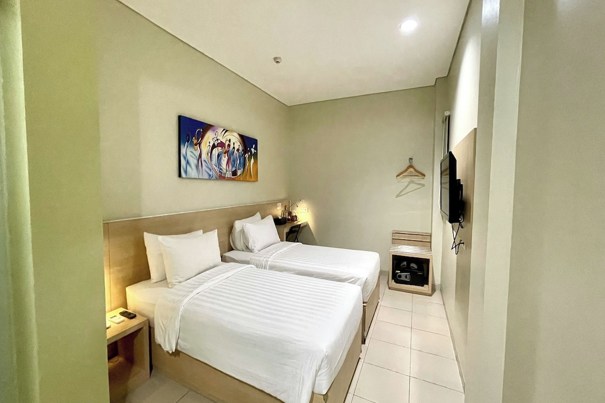A hotel room with two beds, a painting on the wall, a TV, and a small bedside table.