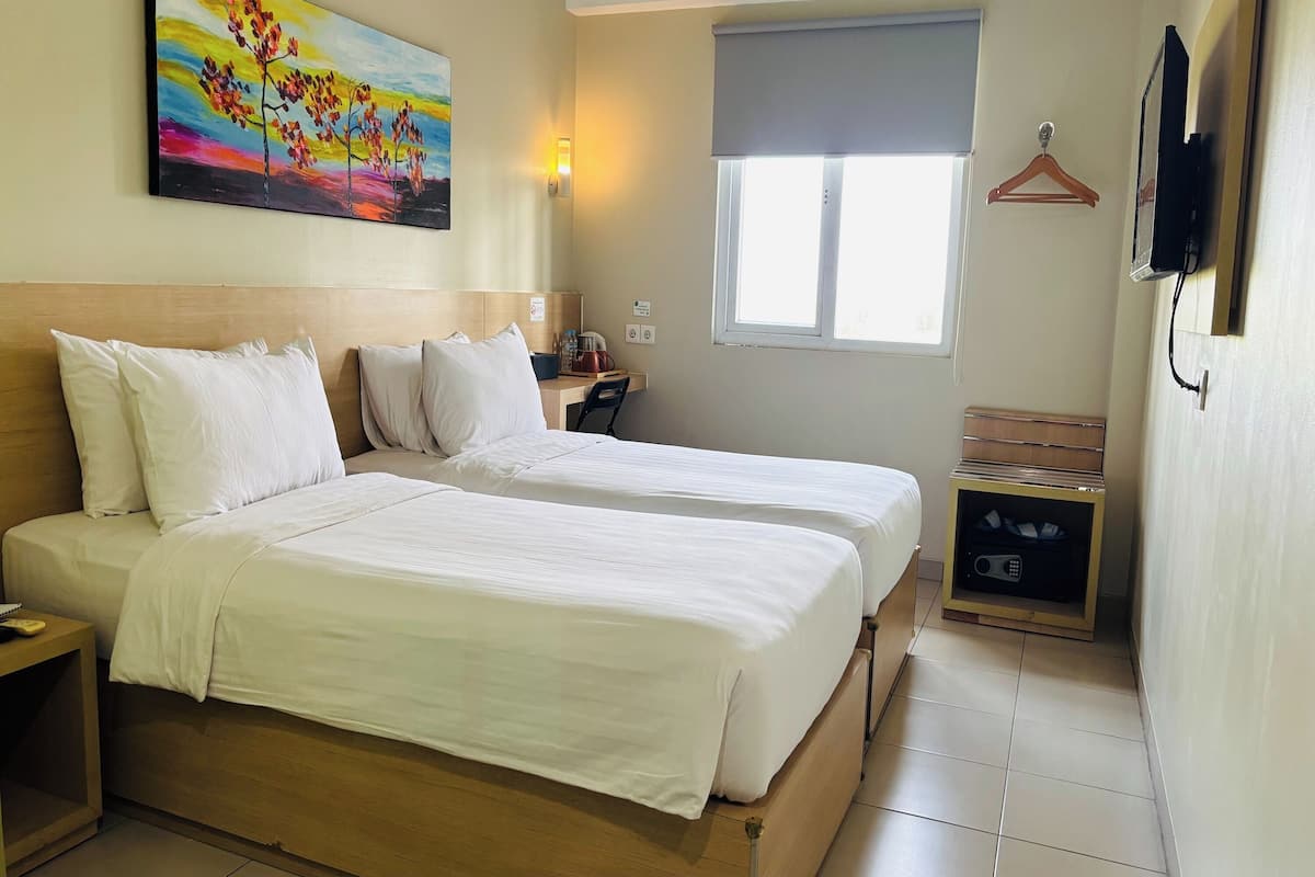 A hotel room with two beds, a painting on the wall, a TV mounted on the wall, and a window with a view.