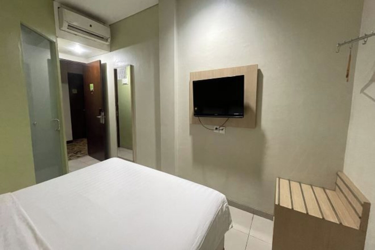 A hotel room with a bed, a mounted TV, and a wooden bench.