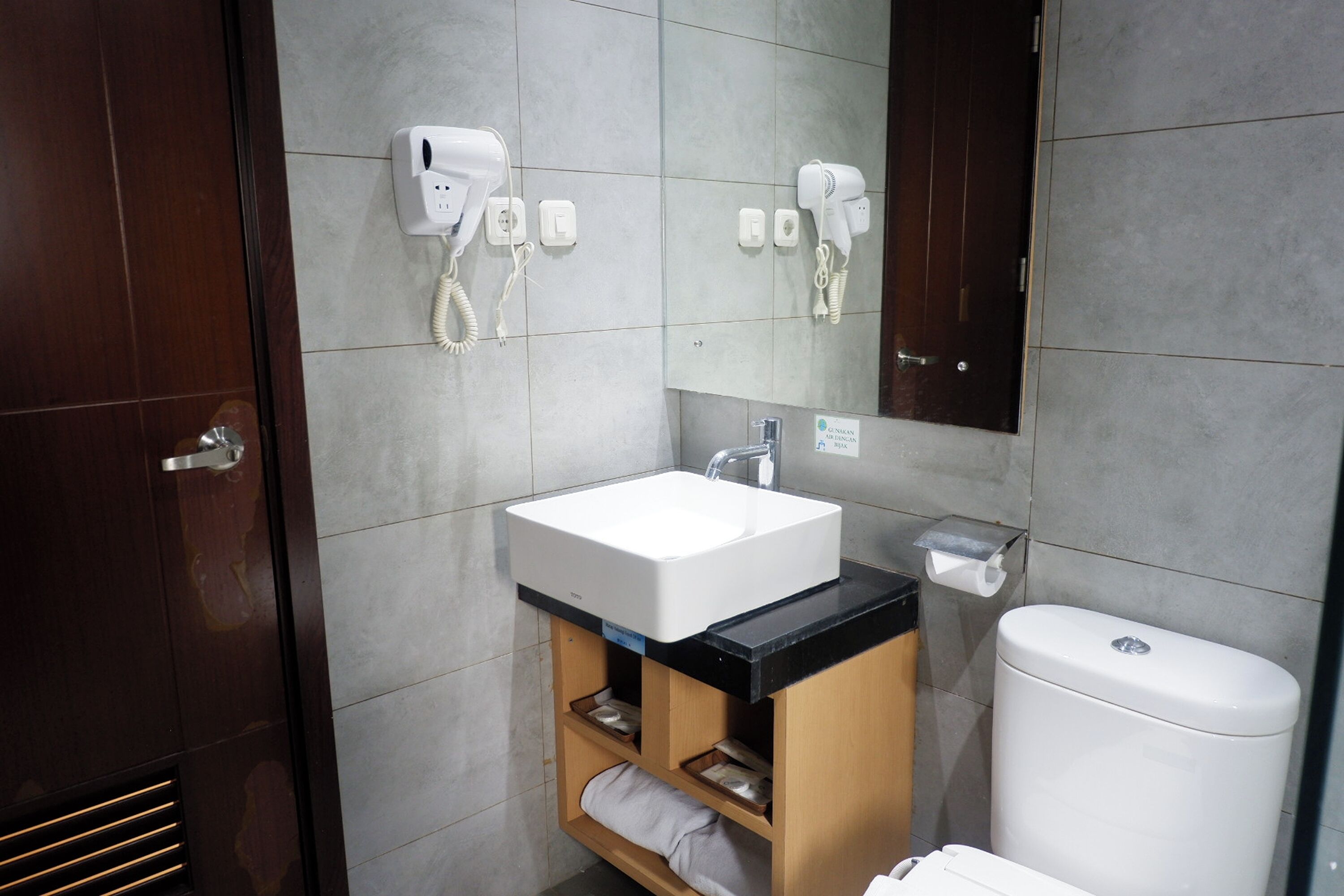 A bathroom with a white sink, a mirror, and two hair dryers mounted on the wall.