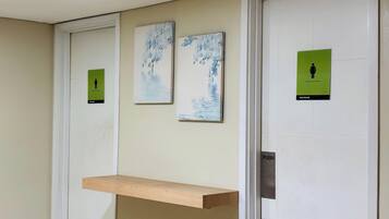 A restroom with a push button, a wooden shelf, and three signs indicating restrooms and a women's restroom.