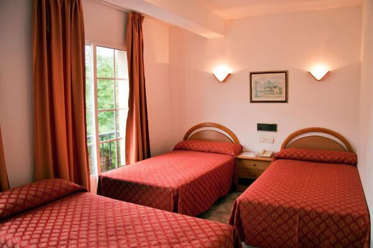 Habitación de hotel con tres camas individuales, una ventana con cortinas, dos lámparas de pared y una mesita con teléfono.