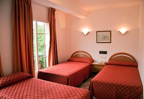 Habitación de hotel con tres camas individuales, una ventana con cortinas, dos lámparas de pared y una mesita con teléfono.