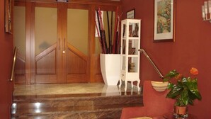 A hotel lobby with a marble staircase, a red armchair, a white cabinet with framed pictures, and a potted plant. - Florida Mar Hotel (Sanxenxo)