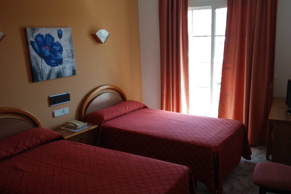 Habitación de hotel con dos camas, un escritorio con computadora, teléfono y un cuadro en la pared.