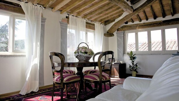 Een kamer met een houten plafond, een eettafel met stoelen, een witte bank en een raam met gordijnen.