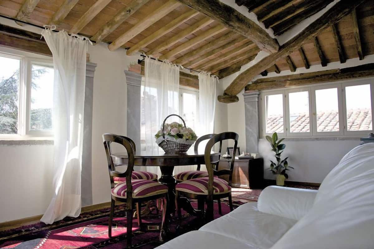 A room with a wooden ceiling, a dining table with chairs, a white sofa, and a window with curtains.