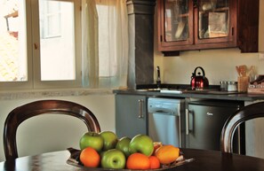 Una cocina con una mesa de comedor dispuesta con fruta, una tetera y armarios.