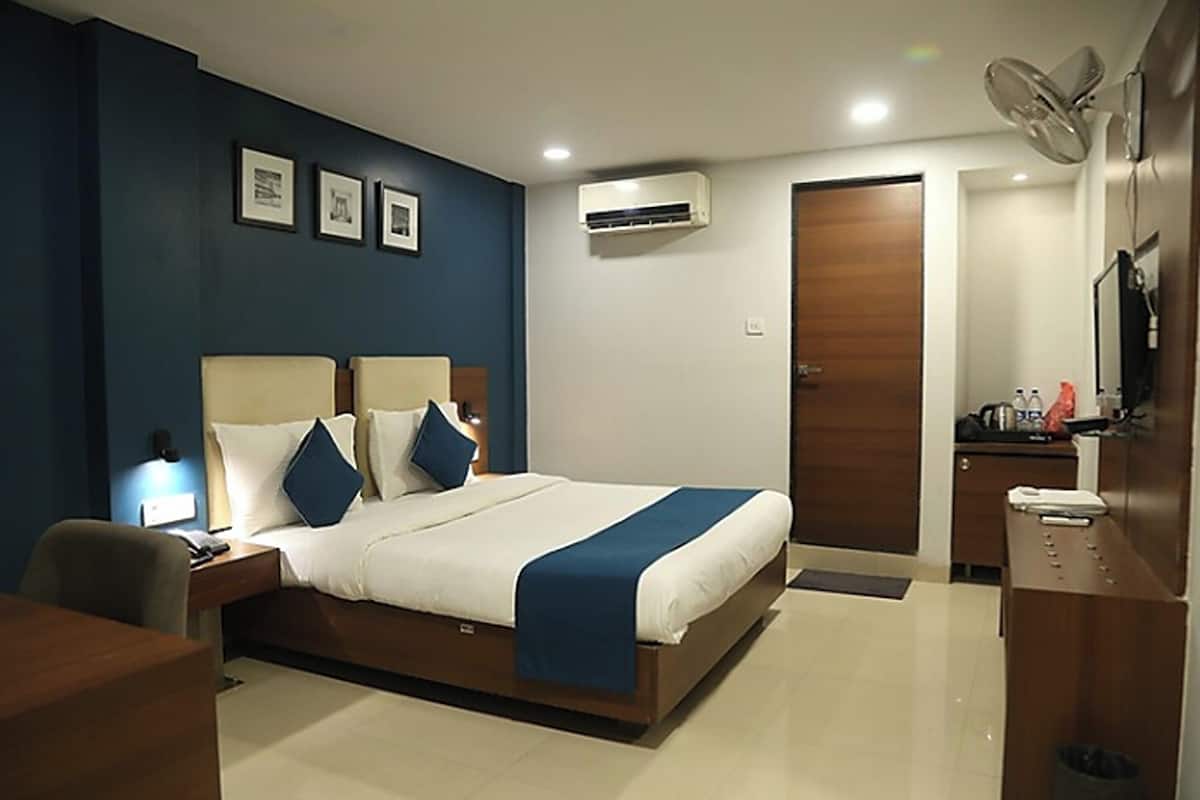 A modern hotel room with a large bed, bedside tables, a desk, and an air conditioning unit.