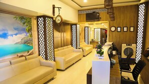 A modern living room with beige sofas, a wooden reception desk, and a large painting of a coastal scene. - Hotel Concord Galaxy (Mumbai)