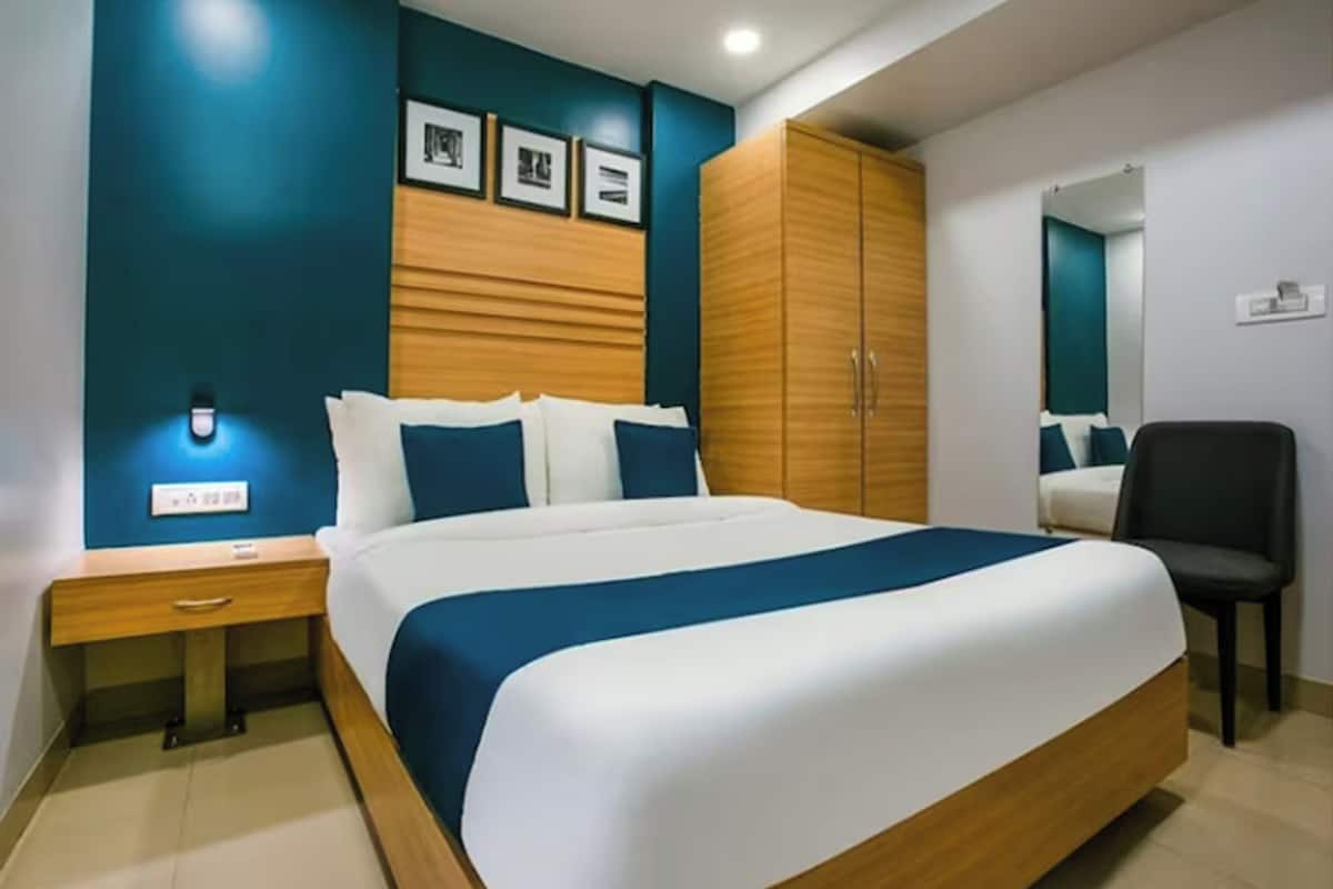 A neatly arranged bedroom with a large bed, a wooden wardrobe, a nightstand, and a chair.