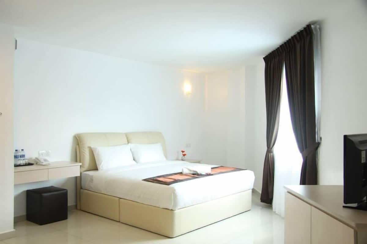 A hotel room with a bed, bedside table, TV, and a window with curtains.
