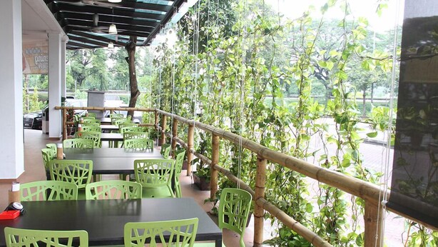 Un área de comedor al aire libre con sillas y mesas verdes, rodeada de barandas de bambú y abundante vegetación.