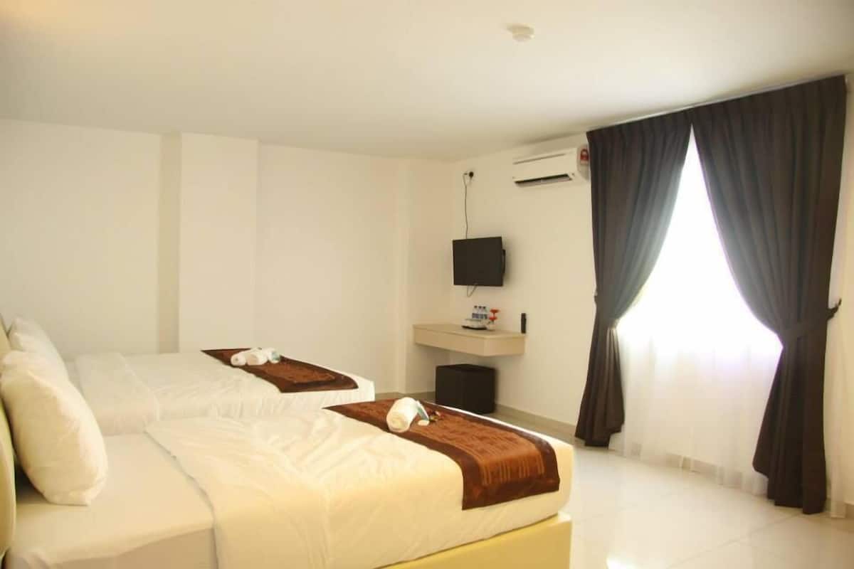 A hotel room with two beds, a TV, a small table with toiletries, and a window with curtains.