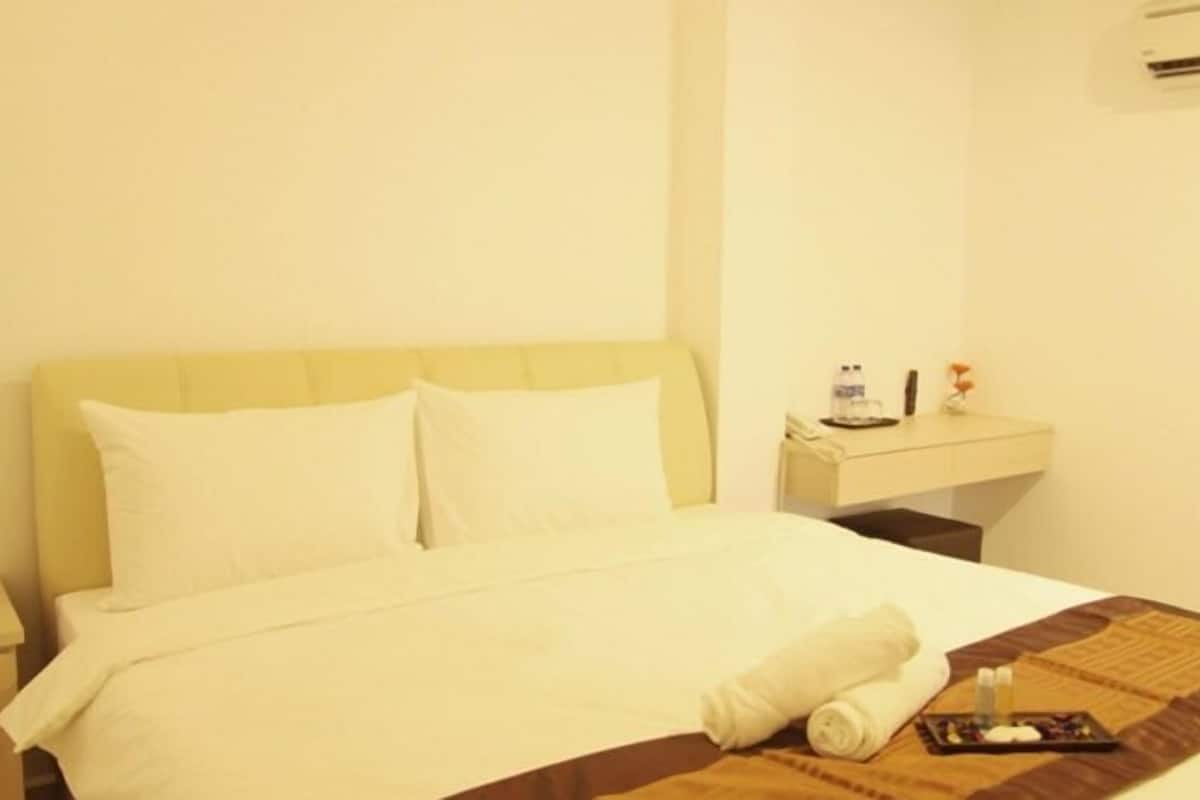 A hotel room with a bed, a bedside table with a bottle and a remote control, and a wall-mounted air conditioner.