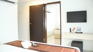 Habitación de hotel con cama, escritorio con televisor de pantalla plana, espejo y armario.