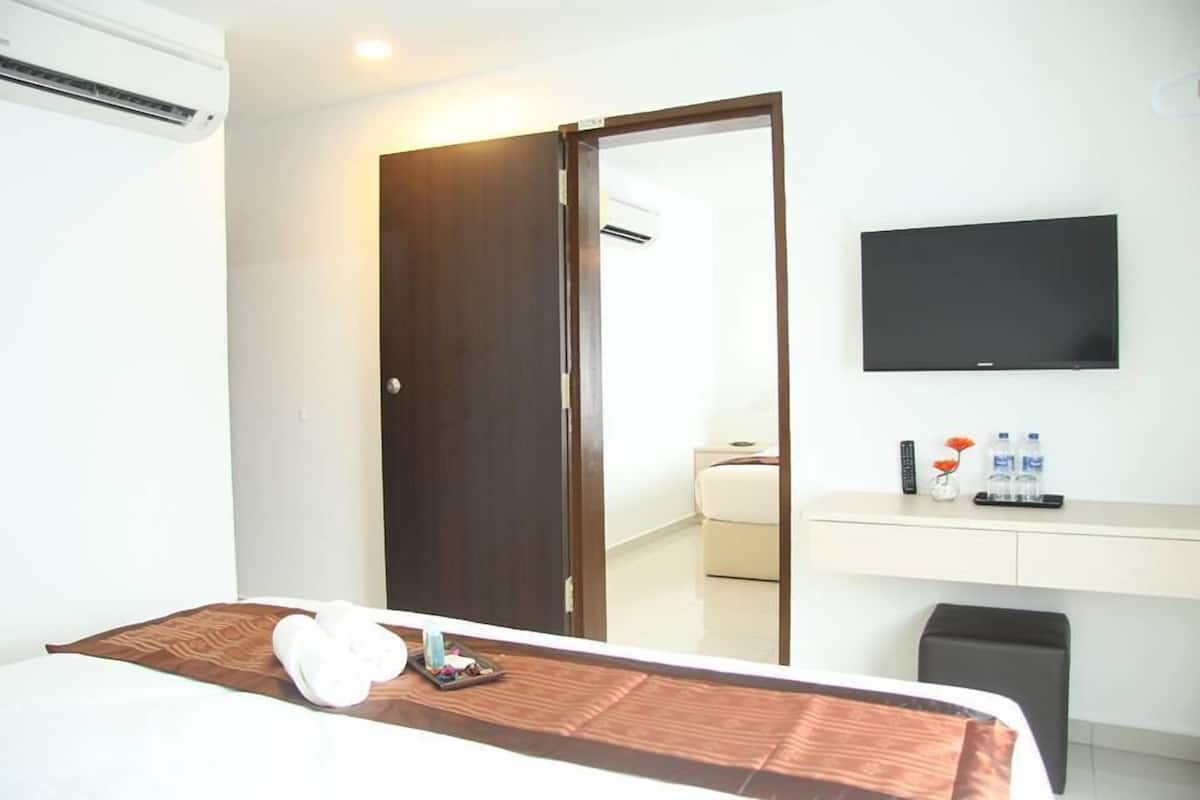 A hotel room with a bed, a desk with a flat-screen TV, a mirror, and a wardrobe.