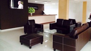 Una moderna zona de recepción con mostrador, dos sofás, una mesa de centro de vidrio y una planta en maceta.