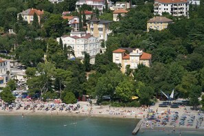 Uma área costeira com praia, vários guarda-sóis e pessoas.