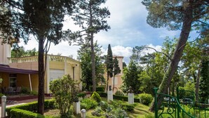 A well-maintained garden with manicured hedges, a variety of trees, and a green metal gate. - Hotel Vila Ruzica (Crikvenica)