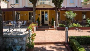 A hotel entrance with a covered patio area, outdoor seating, and potted plants. - Hotel Vila Ruzica (Crikvenica)