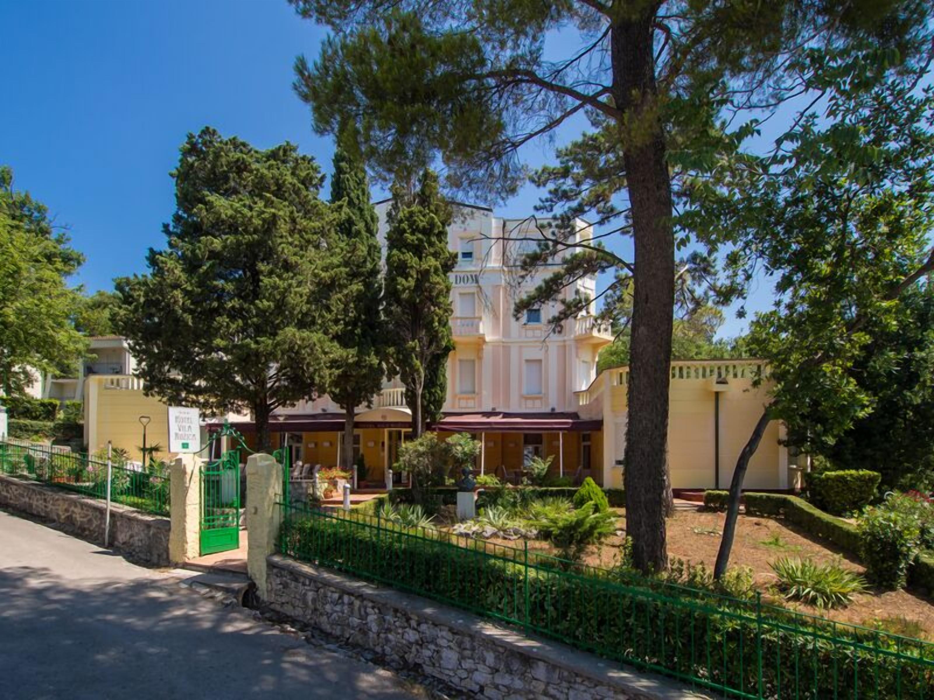 A hotel with a large building, a green fence, and trees.