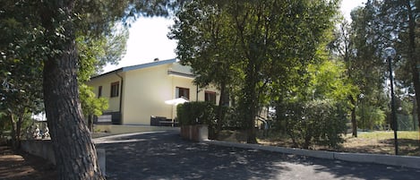 A building with a yellow facade, surrounded by trees and a paved driveway.