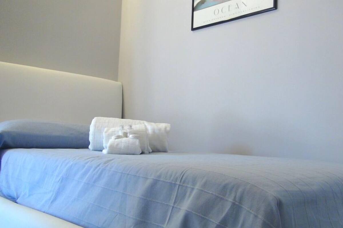 Un lit bien fait, avec une couvre-lit bleue et des oreillers blancs, un tableau encadré accroché au mur et une tête de lit blanche.