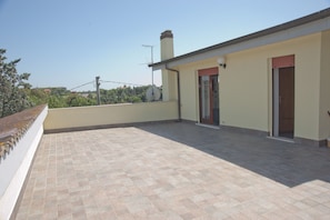 Una terraza en la azotea con suelo de baldosas, una chimenea y una puerta que da a un espacio interior.