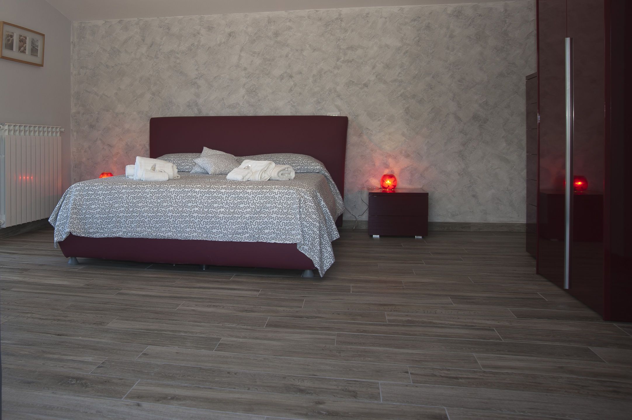 A modern bedroom with a patterned bedspread, a dark headboard, and two bedside tables with red lamps.