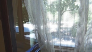A view through a window with vertical blinds, a car parked outside, and a building in the background. - Domus in Viridi (Rome)
