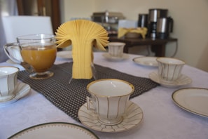 Una mesa de comedor dispuesta con platos blancos y dorados, tazas y un vaso de zumo de naranja.