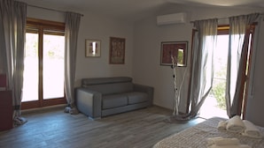 A bedroom with a grey sofa, a bed with towels, a standing lamp, and two framed pictures on the wall. - Domus in Viridi (Rome)