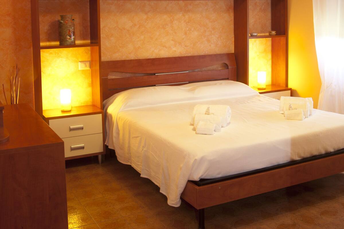 Un lit bien fait, avec du linge de lit et des serviettes blanches, une tête de lit en bois et des lampes de chevet.