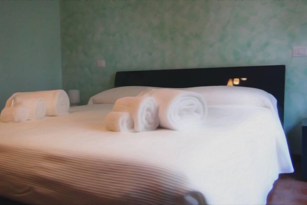 Un lit bien fait, avec du linge de lit blanc et des serviettes pliées, une tête de lit sombre et un mur vert.